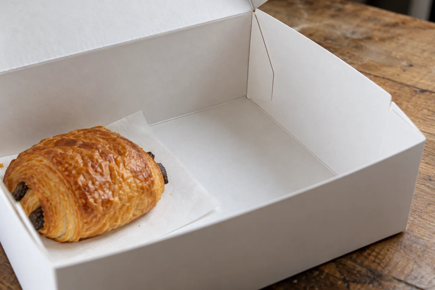 Fond et angle intérieur d’une boîte ouverte, près d’une pâtisserie sur papier.